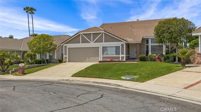 english style home featuring an attached garage, a tile roof, stucco siding, a front yard, and concrete driveway