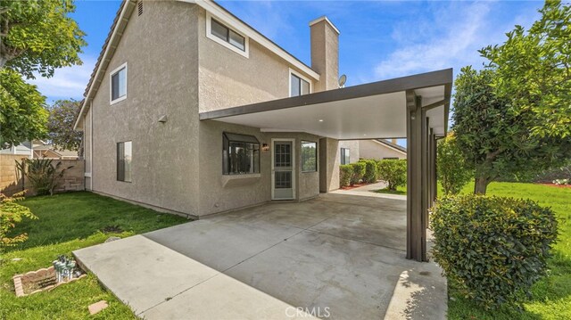 rear view of property featuring fence, stucco siding, a chimney, a patio area, and a lawn