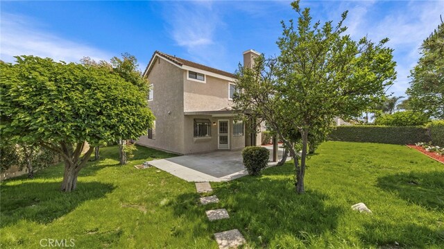 rear view of property featuring a patio area, stucco siding, a yard, and a chimney