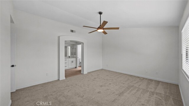 unfurnished bedroom with visible vents, light colored carpet, arched walkways, baseboards, and ensuite bathroom