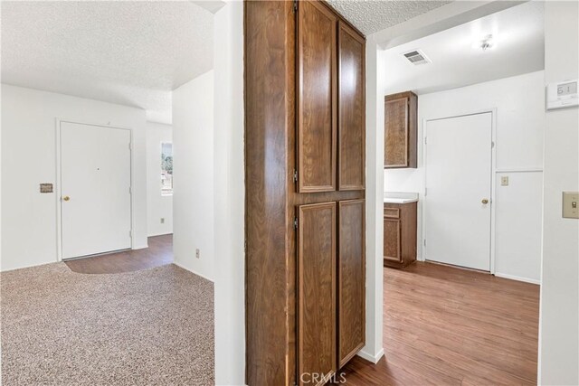 hallway featuring visible vents, a textured ceiling, and light wood-style floors
