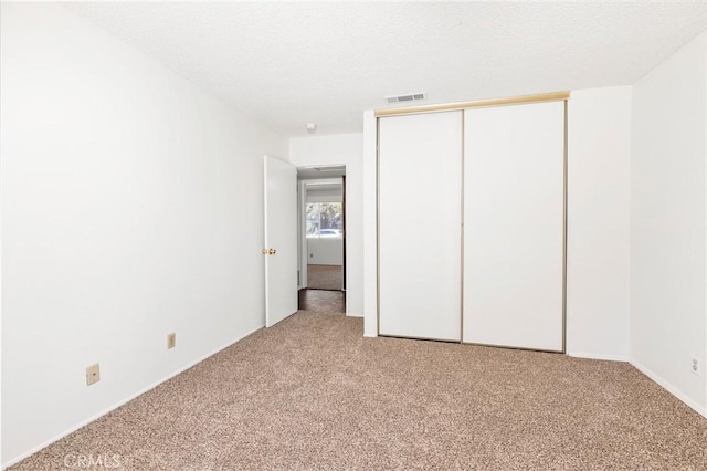 unfurnished bedroom with a textured ceiling, a closet, visible vents, and light colored carpet
