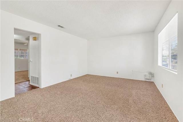 empty room with carpet, visible vents, and plenty of natural light