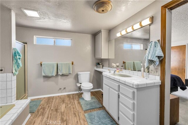 bathroom featuring a shower with door, wood finished floors, toilet, a wealth of natural light, and a textured ceiling