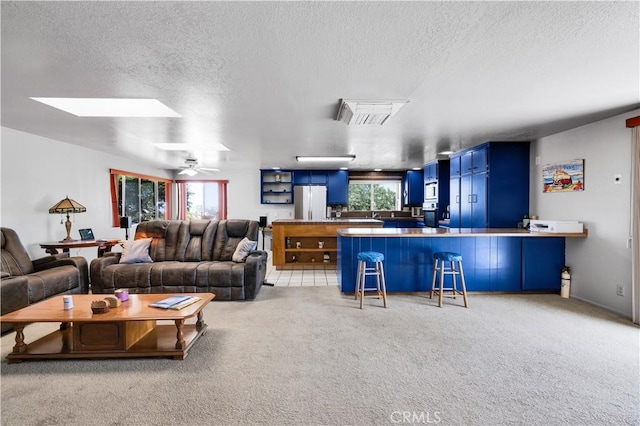 living room with light carpet, a ceiling fan, a textured ceiling, and a skylight