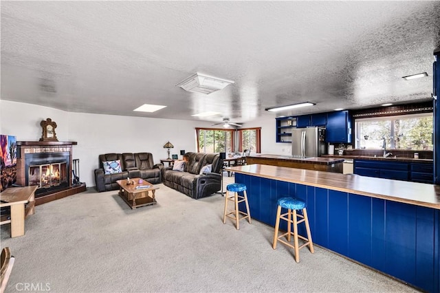 living room with a tiled fireplace, carpet floors, a textured ceiling, and a healthy amount of sunlight
