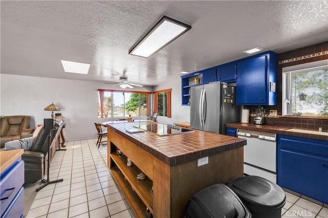 kitchen with black electric cooktop, freestanding refrigerator, white dishwasher, blue cabinetry, and open shelves