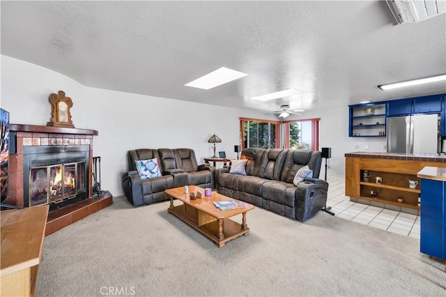 living area with a tiled fireplace, a skylight, light colored carpet, light tile patterned floors, and ceiling fan