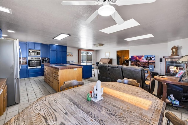 dining area with a textured ceiling, a ceiling fan, a skylight, and light tile patterned floors