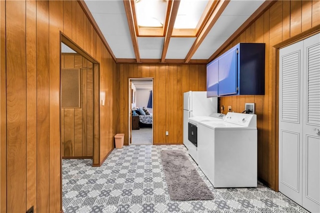 clothes washing area with separate washer and dryer, wood walls, light floors, and cabinet space