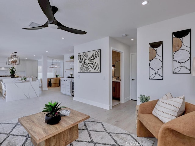 living area with light wood-type flooring, baseboards, recessed lighting, and ceiling fan with notable chandelier