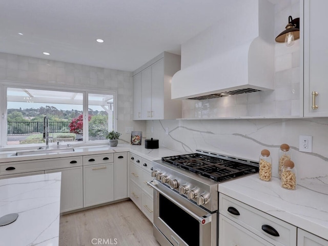 kitchen with white cabinets, high end stainless steel range, a sink, light wood-type flooring, and custom exhaust hood