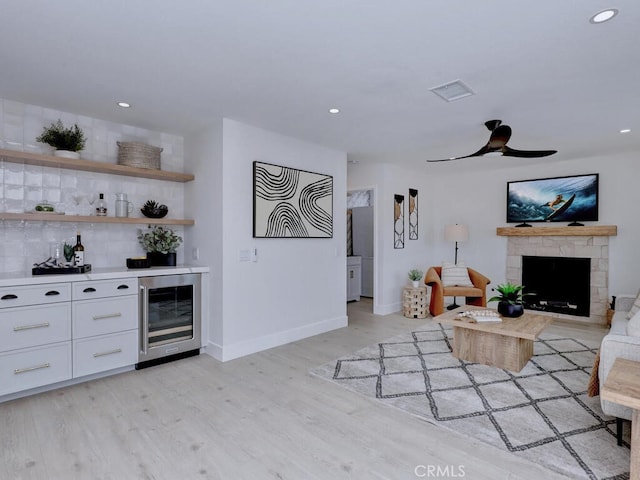 living area featuring a bar, light wood finished floors, a fireplace, baseboards, and wine cooler