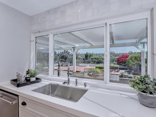 kitchen with light countertops, dishwasher, white cabinetry, and a sink