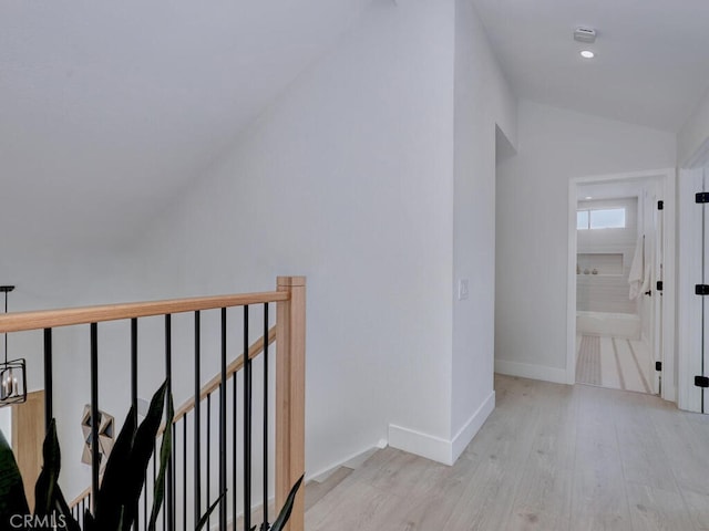 hall featuring an upstairs landing, light wood-style floors, vaulted ceiling, and baseboards