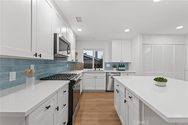 kitchen with a sink, stainless steel appliances, light countertops, recessed lighting, and backsplash