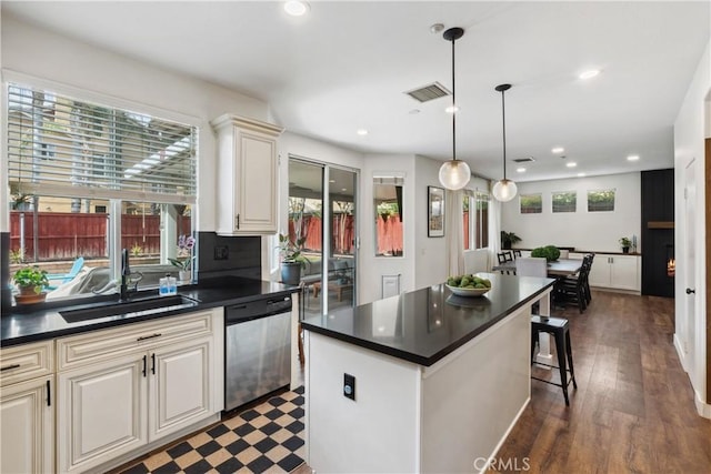 kitchen with stainless steel dishwasher, a sink, a healthy amount of sunlight, dark countertops, and visible vents