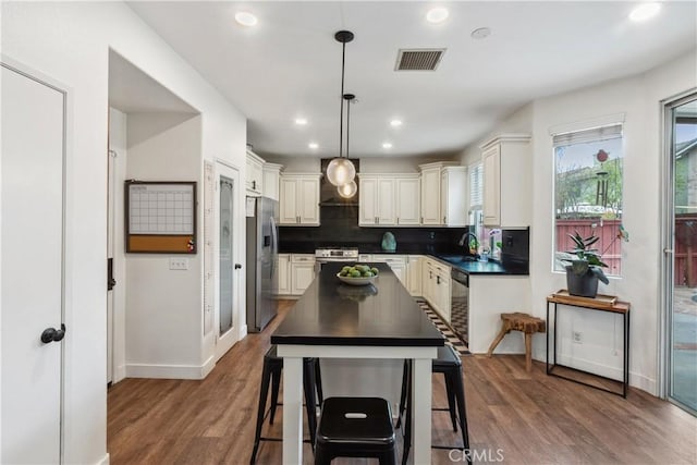 kitchen featuring stainless steel appliances, dark countertops, wood finished floors, a sink, and baseboards