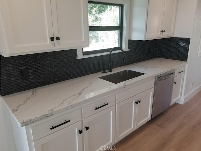 kitchen with white cabinets, a sink, light wood-type flooring, light stone counters, and dishwasher