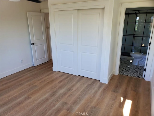 unfurnished bedroom with wood finished floors, a closet, baseboards, and ensuite bathroom