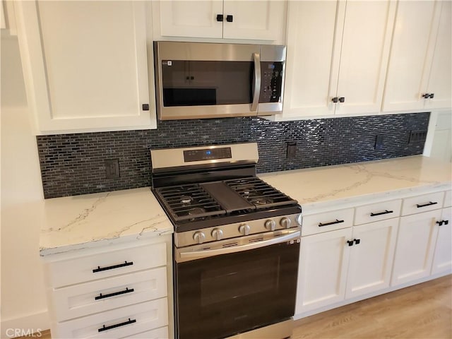 kitchen with white cabinets, light wood finished floors, light stone countertops, decorative backsplash, and appliances with stainless steel finishes