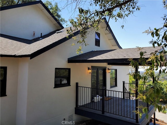 back of house with stucco siding, a shingled roof, and french doors