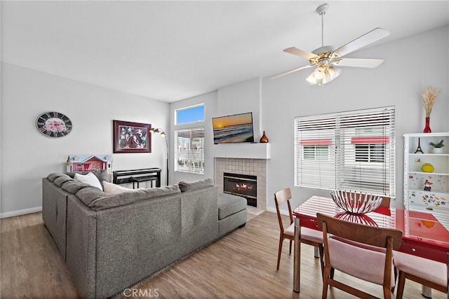 living area featuring a fireplace, wood finished floors, ceiling fan, and baseboards