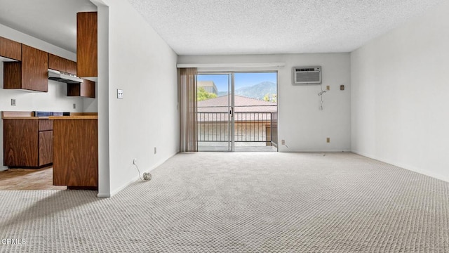 unfurnished living room with light colored carpet, a wall unit AC, a textured ceiling, and baseboards