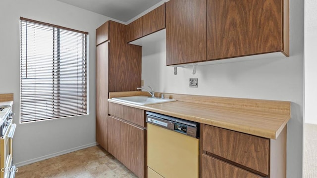 kitchen featuring baseboards, dishwasher, light countertops, and a sink