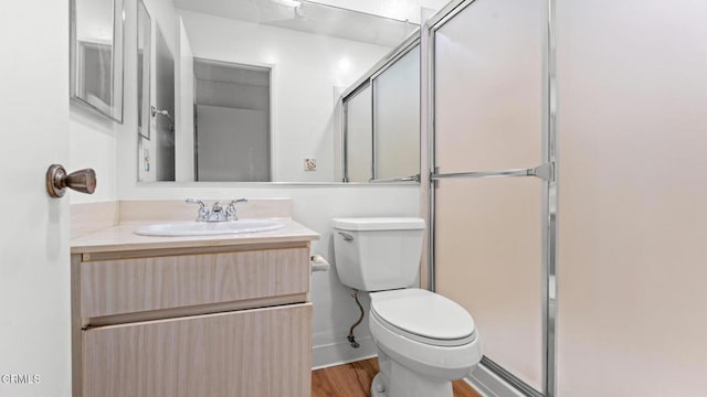 full bath with toilet, a shower with shower door, wood finished floors, and vanity