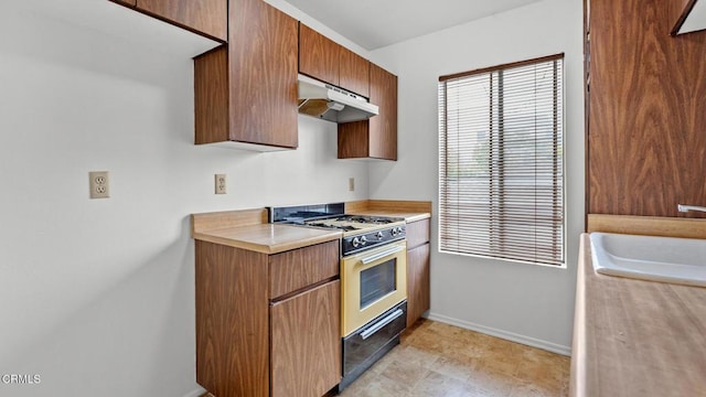 kitchen featuring a sink, light countertops, gas range, baseboards, and under cabinet range hood