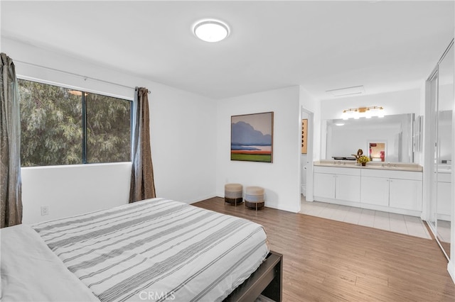 bedroom with a sink, baseboards, ensuite bathroom, and light wood-type flooring
