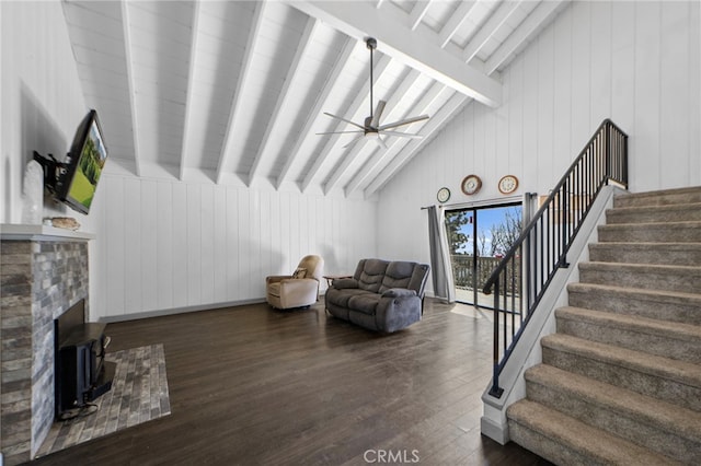 living area with stairway, lofted ceiling with beams, dark wood-type flooring, wooden walls, and a ceiling fan