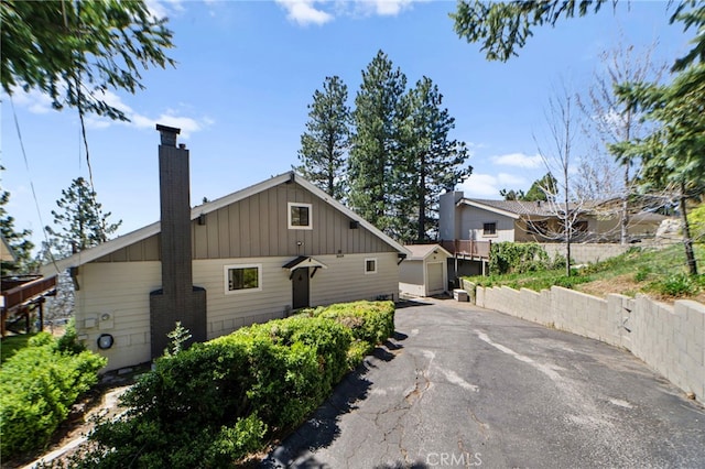 bungalow with a chimney, board and batten siding, aphalt driveway, and a detached garage