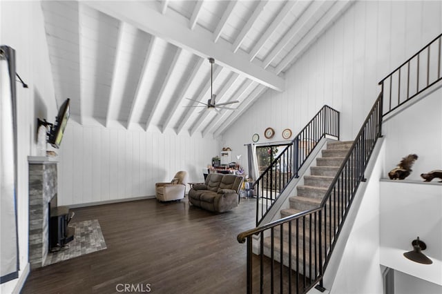 staircase with wooden walls, wood finished floors, lofted ceiling with beams, and a ceiling fan