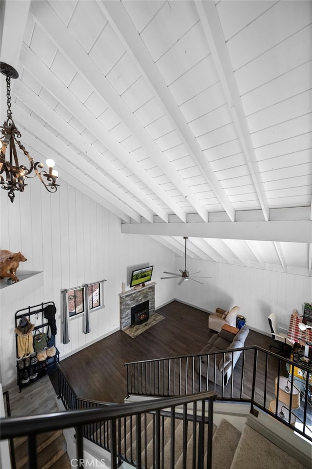 interior space featuring vaulted ceiling with beams, ceiling fan with notable chandelier, wood finished floors, wood walls, and a fireplace