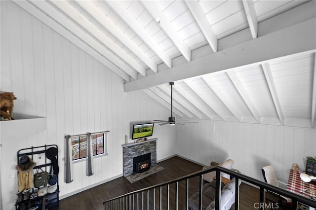 stairway featuring lofted ceiling with beams, wood finished floors, ceiling fan, a stone fireplace, and wooden walls