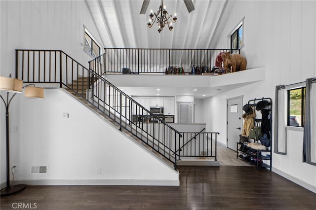 stairway featuring wood finished floors, visible vents, high vaulted ceiling, and a chandelier