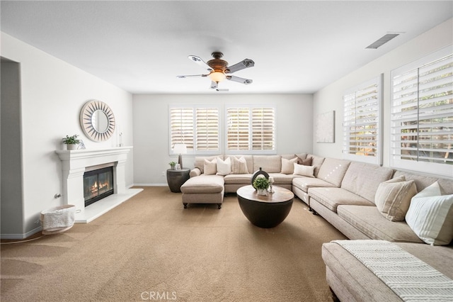 living area with carpet floors, a glass covered fireplace, baseboards, visible vents, and a ceiling fan