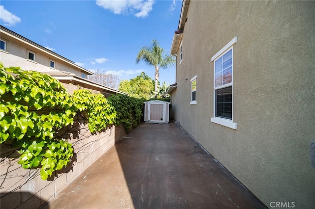 view of side of property with an outdoor structure, a shed, stucco siding, and a patio area