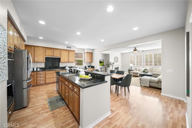 kitchen featuring appliances with stainless steel finishes, light wood-style floors, ceiling fan, and a center island with sink