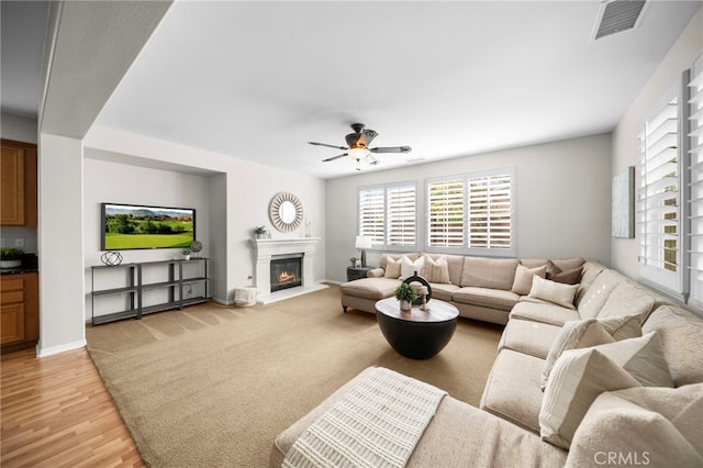 living room featuring a wealth of natural light, a glass covered fireplace, a ceiling fan, and visible vents