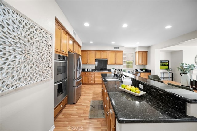 kitchen with a sink, appliances with stainless steel finishes, light wood-style floors, a large island, and recessed lighting