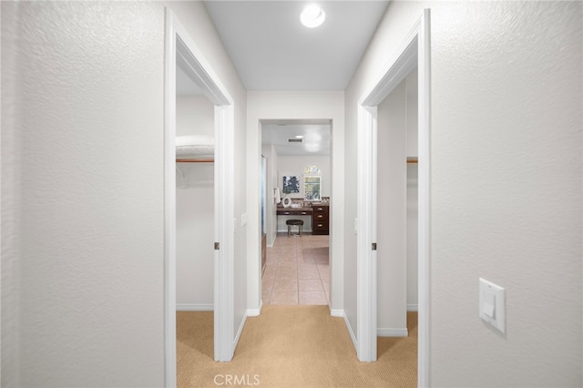 hall with baseboards, light tile patterned floors, and light colored carpet