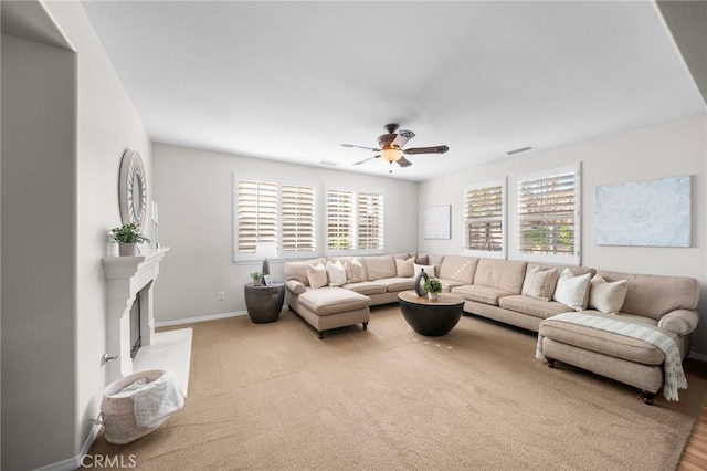 living room with ceiling fan, a fireplace with raised hearth, visible vents, and baseboards