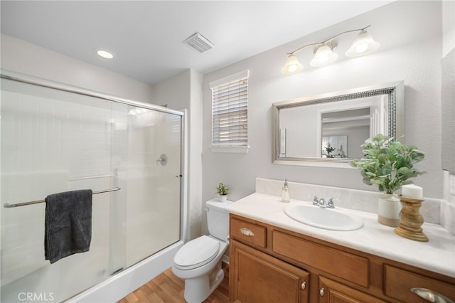 bathroom with wood finished floors, a shower stall, toilet, vanity, and visible vents