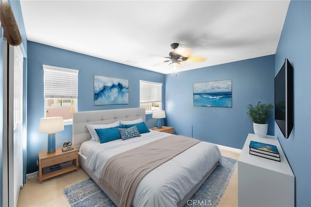 carpeted bedroom with ceiling fan, baseboards, and multiple windows