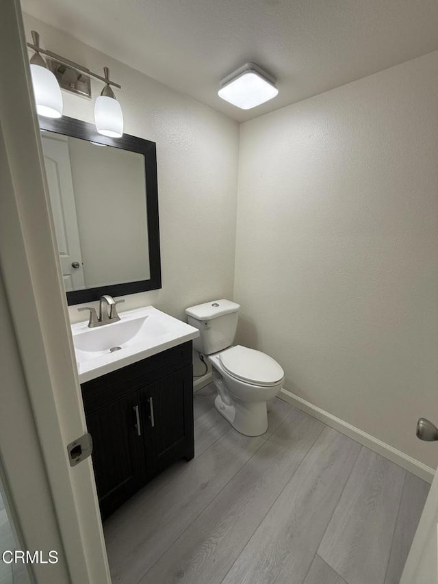 half bathroom with wood finished floors, toilet, vanity, and baseboards