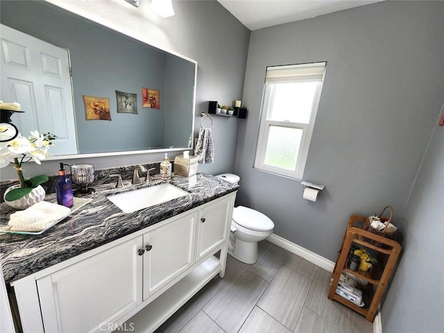 half bath featuring vanity, baseboards, and toilet