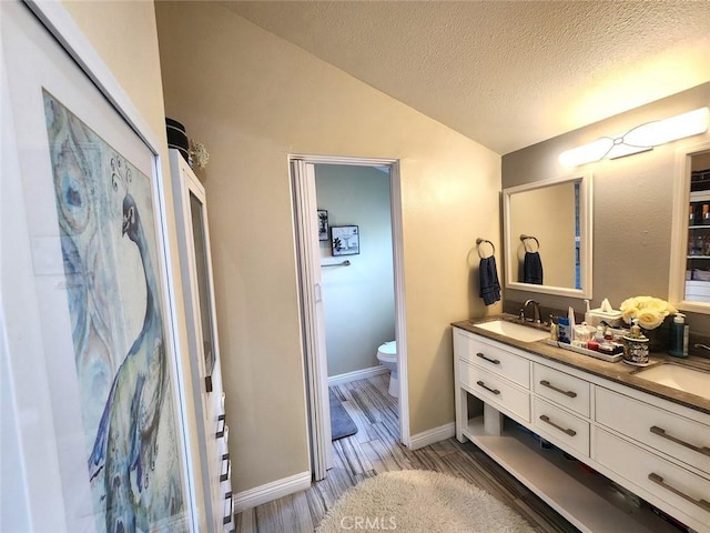 bathroom with a textured ceiling, wood finished floors, vanity, toilet, and lofted ceiling
